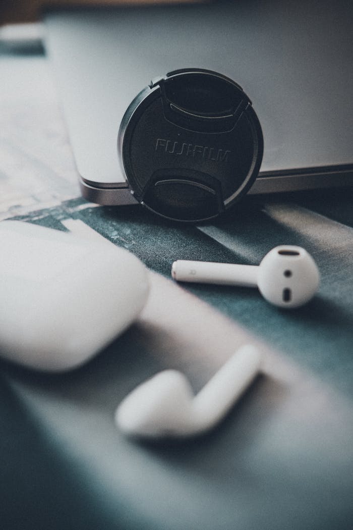 Close-up view of wireless earbuds and a camera lens cap on a table indoors.