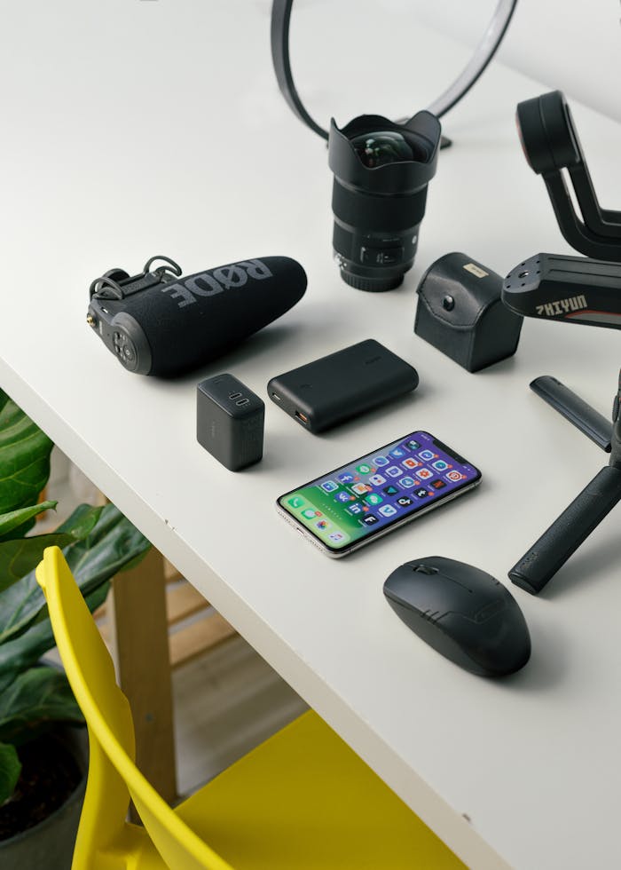 A neat arrangement of various tech devices on a white desk, featuring a smartphone, camera gear, and accessories.