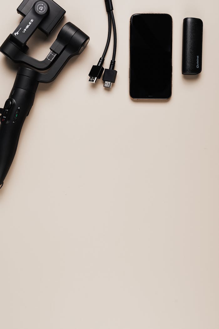 Flat lay of smartphone, gimbal, cables, and accessory on beige surface.