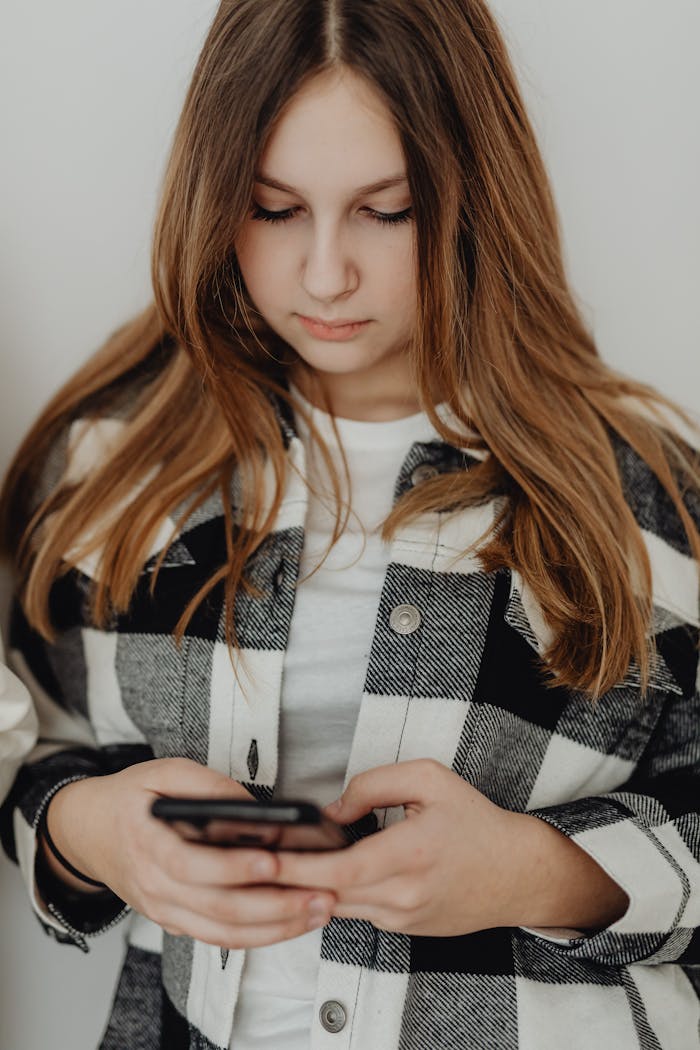 Teenage girl in a plaid shirt focused on her smartphone indoors.
